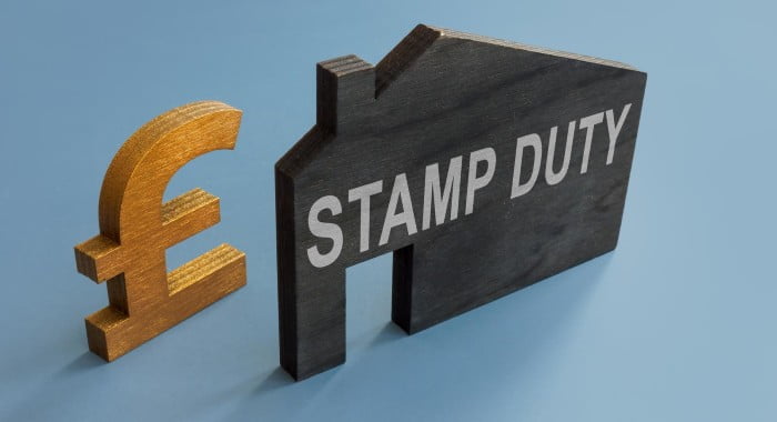 a black house-shaped piece of wood with the words "stamp duty" on it net to a wooden pound sign.